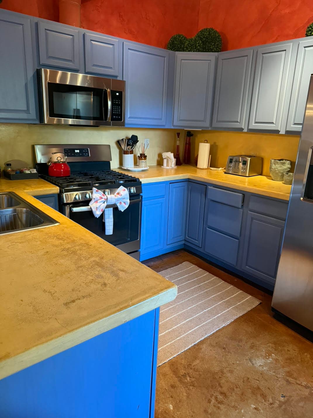 A colorful kitchen featuring blue cabinets, stainless steel appliances, and a striped rug.
