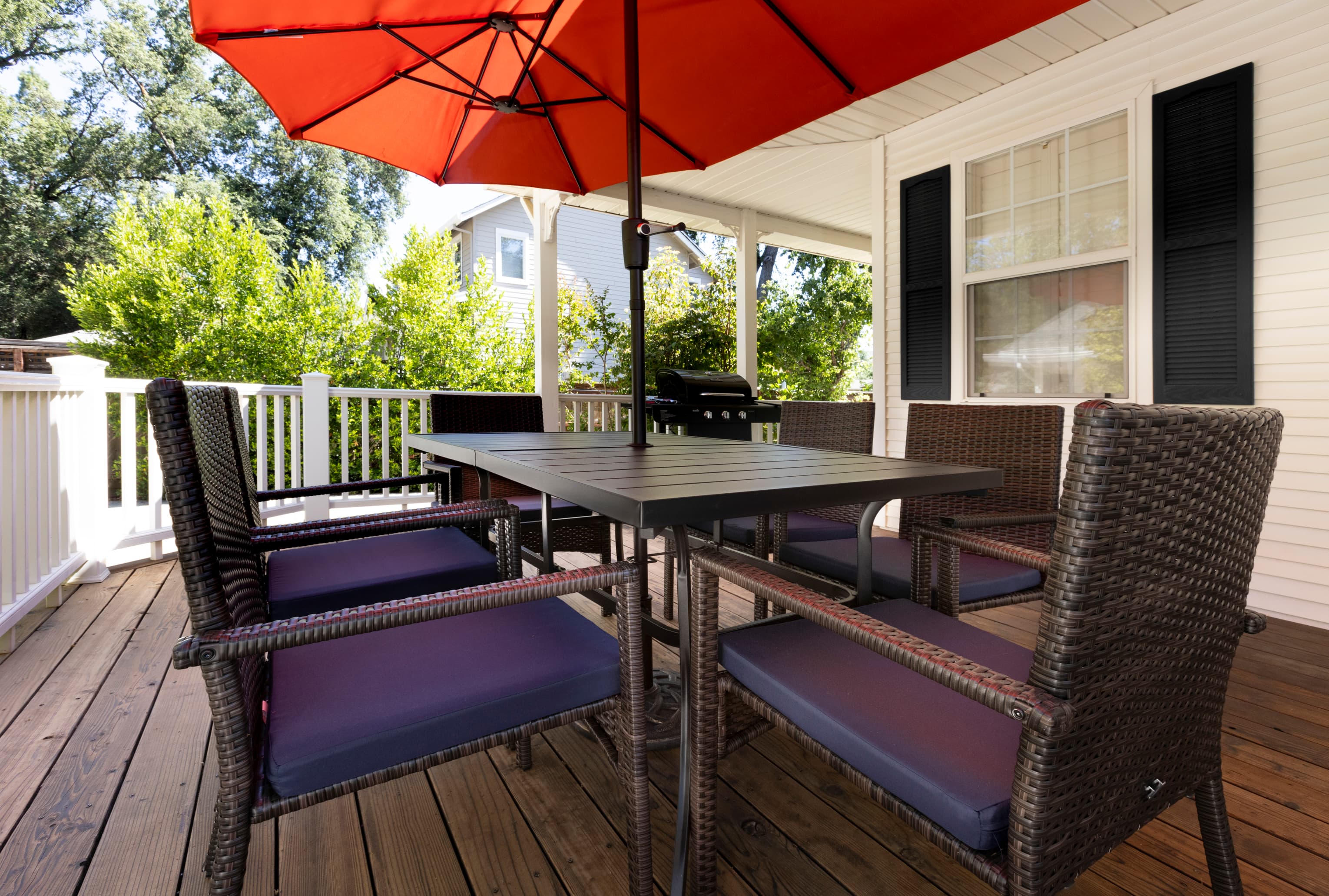 A patio with a table and chairs shaded by a red umbrella.