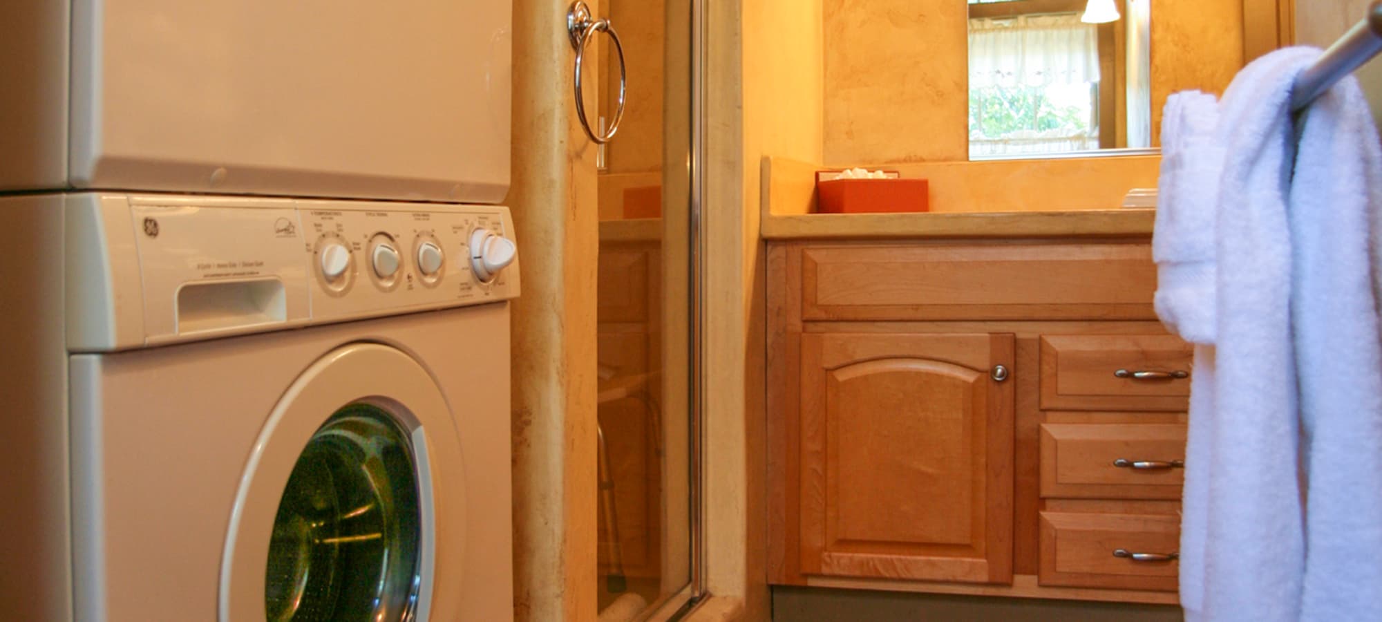 A laundry area featuring a washer next to a wooden vanity and a glass shower.