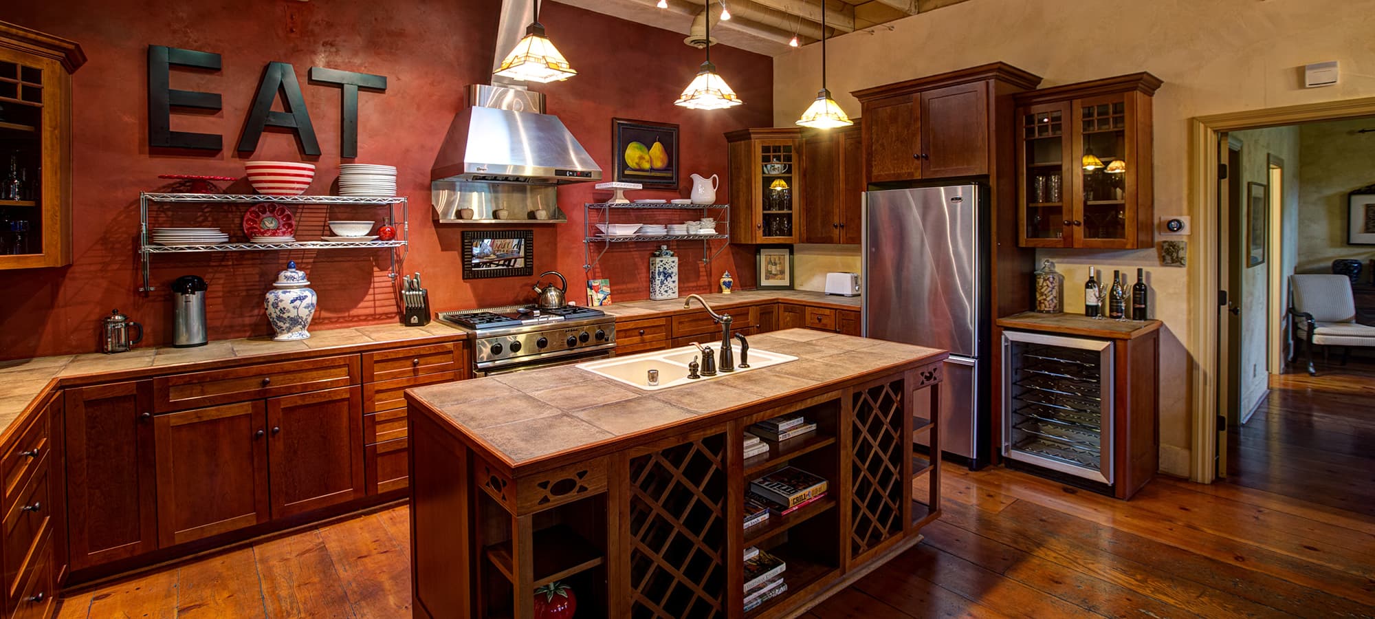 Modern kitchen with wooden cabinets, a large island, and the word "EAT" prominently displayed on the wall.