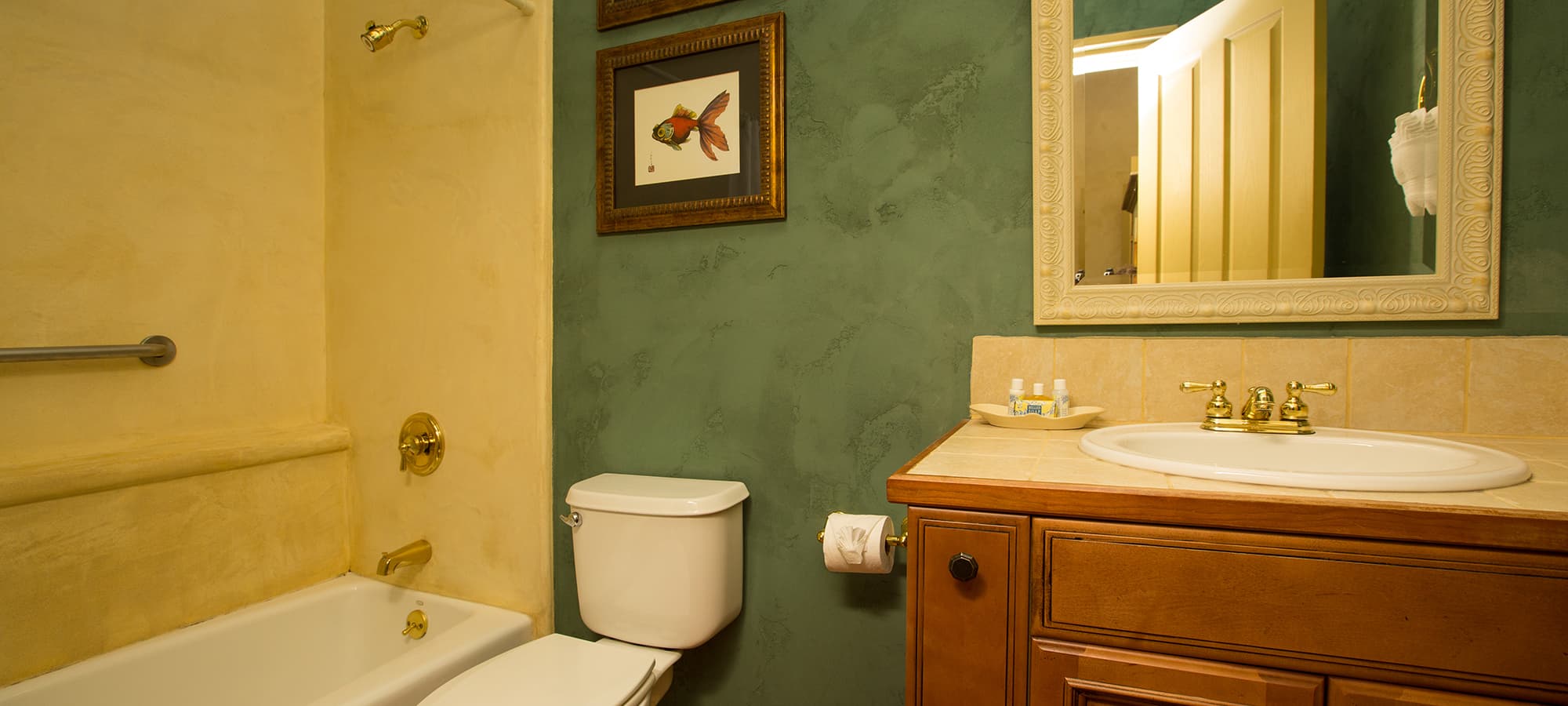 A cozy bathroom featuring a bathtub, toilet, and wooden vanity with a mirror and decorative artwork.