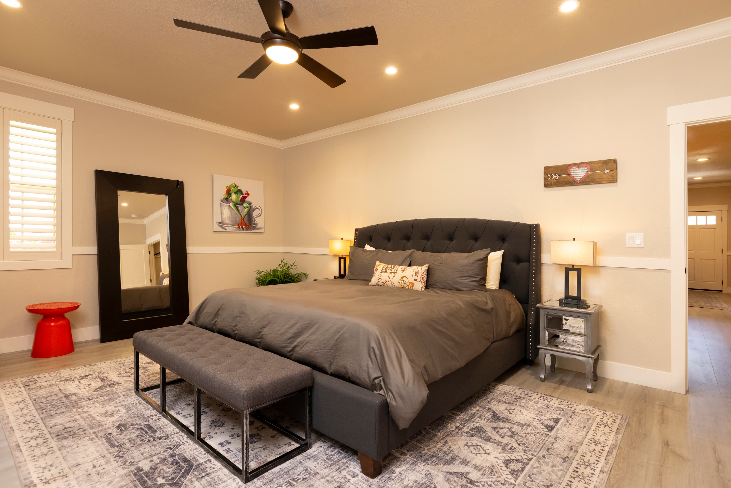 A stylish bedroom featuring a queen-sized bed, a bench at the foot, and elegant decor with a ceiling fan and art on the walls.