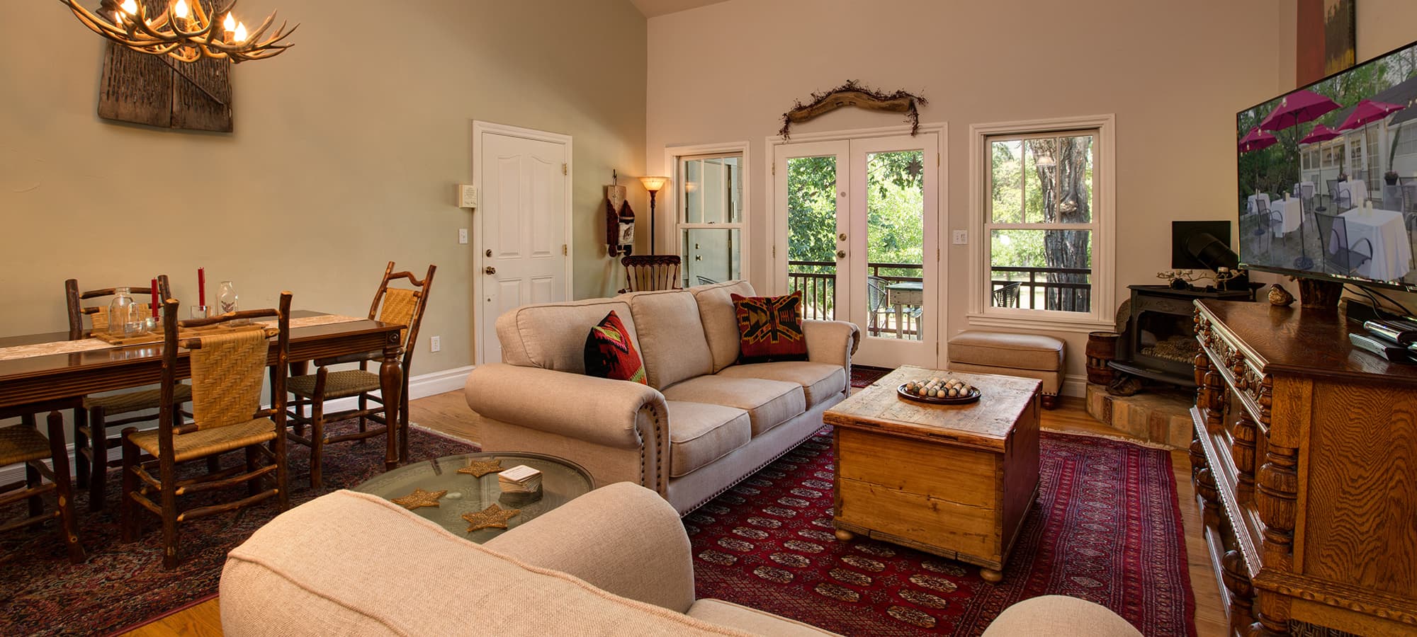 A cozy living room featuring a sofa, wooden coffee table, dining area, and large windows overlooking greenery.