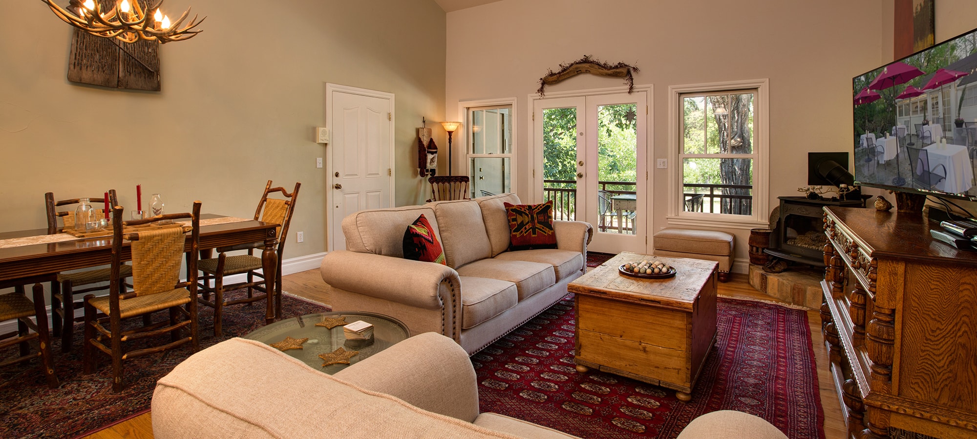 A cozy living room featuring a sofa, wooden coffee table, dining area, and large windows overlooking greenery.