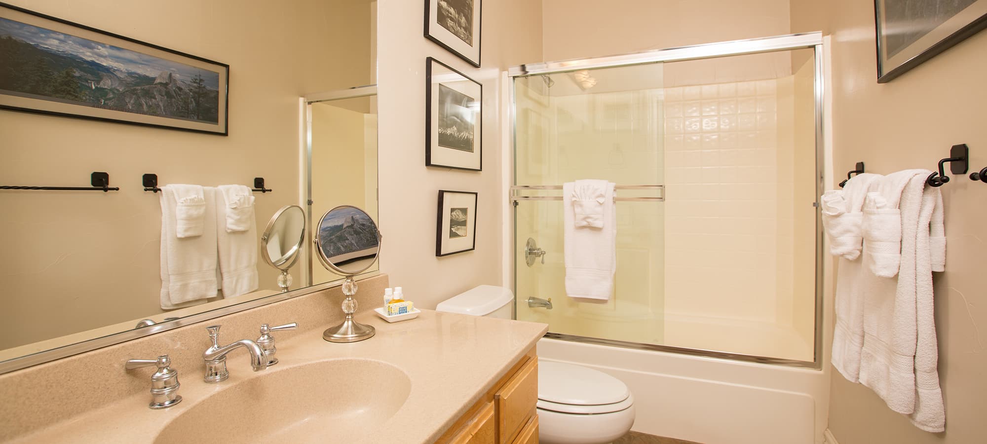 A clean bathroom featuring a sink, mirror, and shower with glass doors, adorned with wall art and neatly arranged towels.