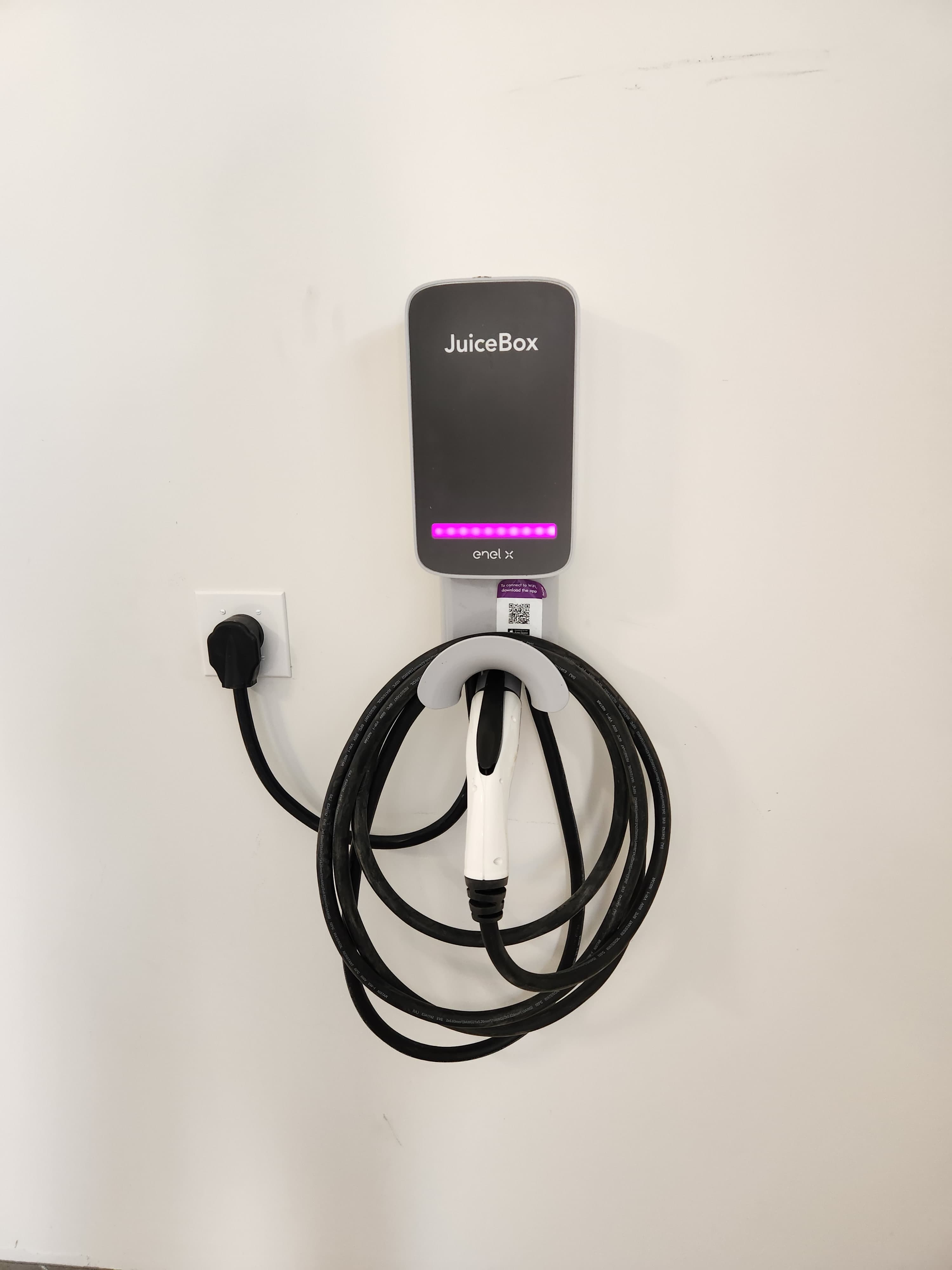 A JuiceBox electric vehicle charger mounted on a wall with a coiled charging cable.