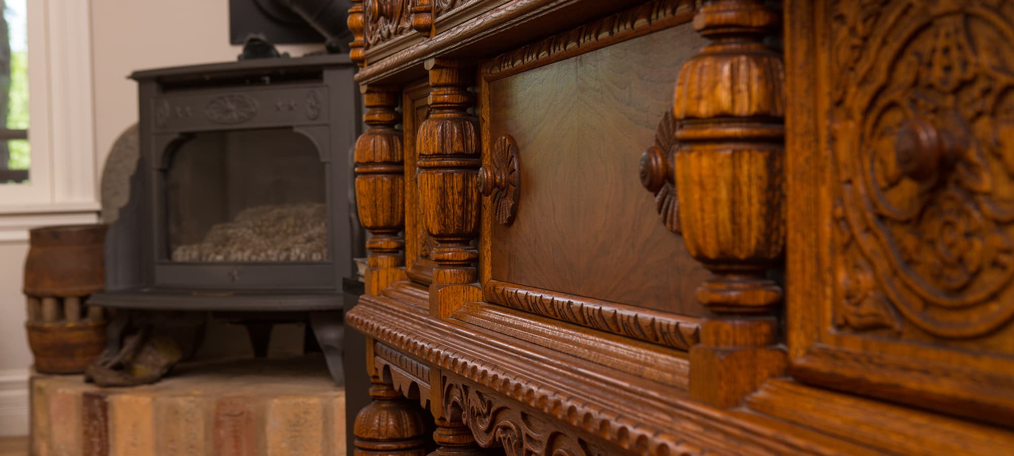 A carved wooden chest with ornate details in the foreground and a wood stove in the background.