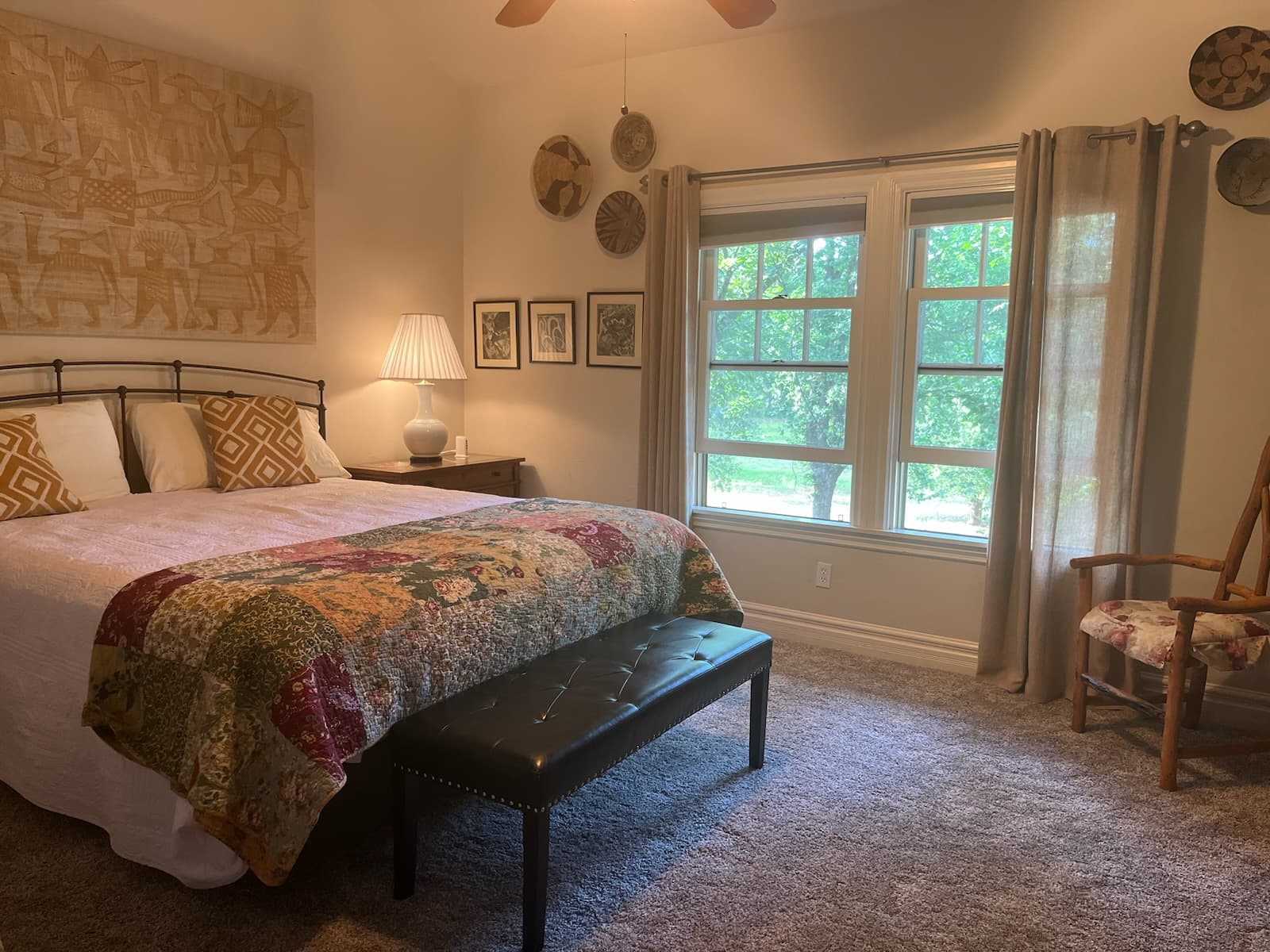 A cozy bedroom featuring a bed with a patterned quilt, a bench at the foot, and windows allowing natural light to fill the space.