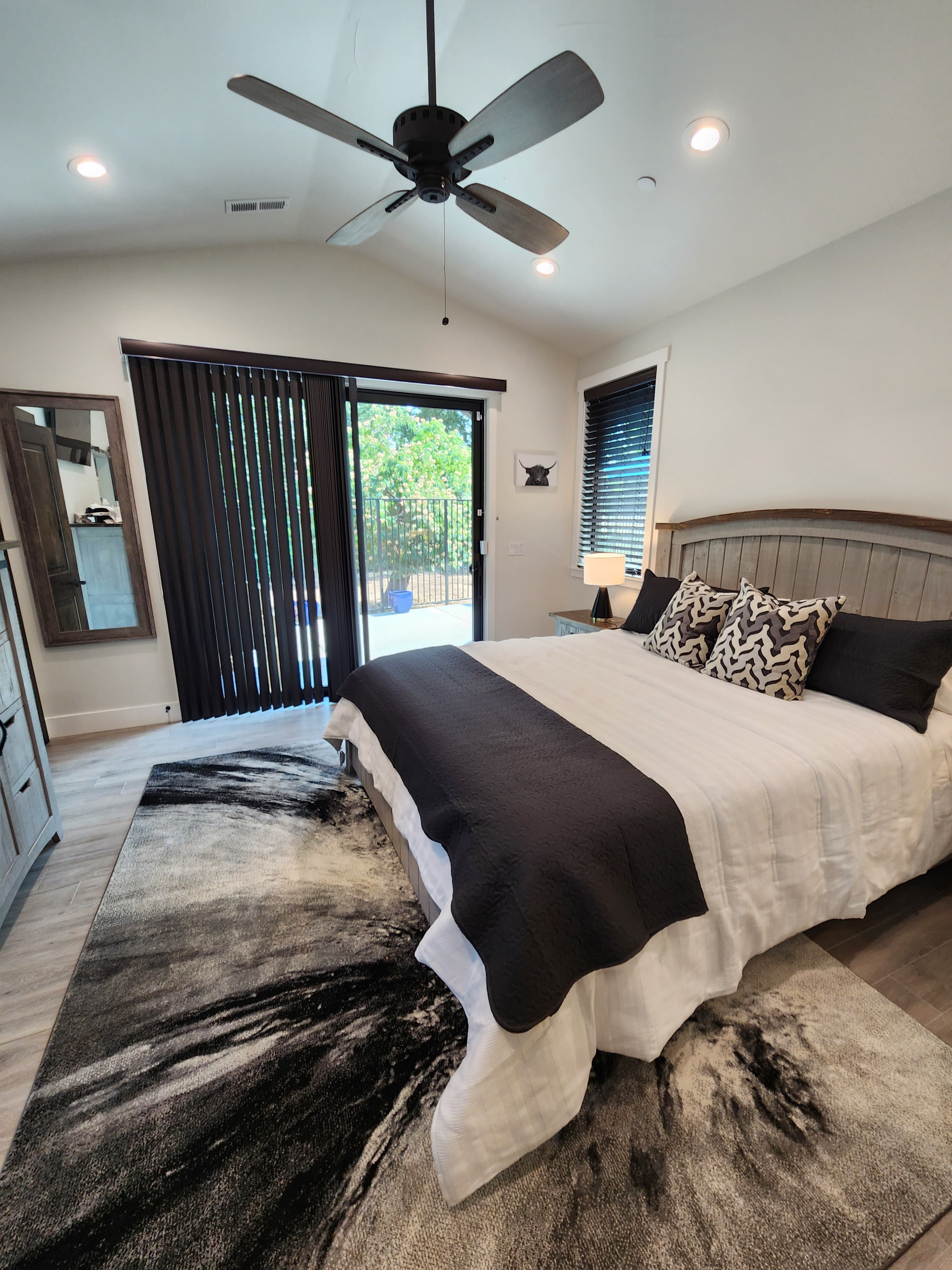 A modern bedroom featuring a king-sized bed, dark bedding, a ceiling fan, and sliding glass doors leading to an outdoor space.