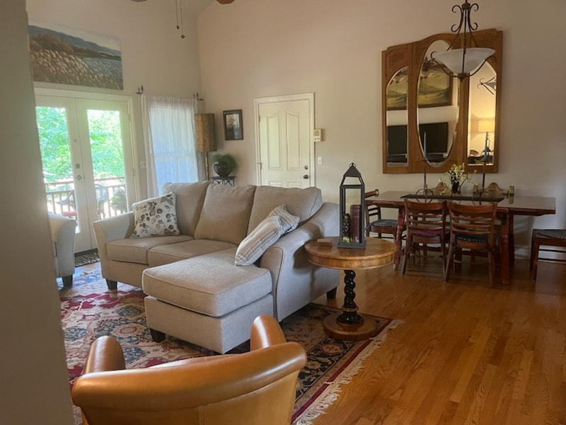 A cozy living room featuring a sectional sofa, a wooden dining table, and large windows with natural light.