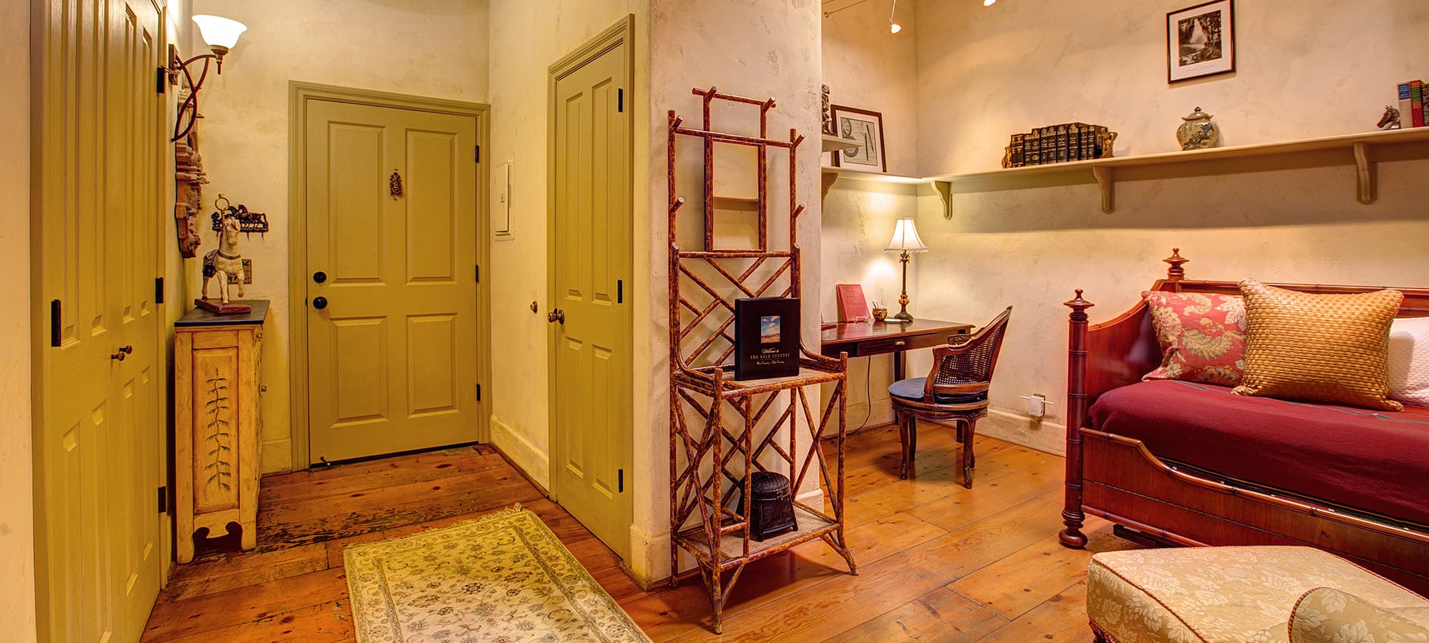 A cozy room featuring a red bed, desk, bookshelves, and soft lighting.