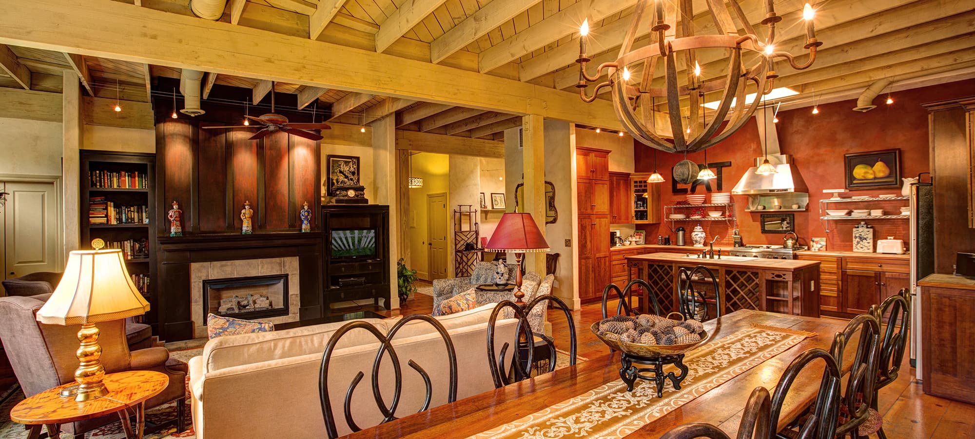 A spacious living area featuring a cozy seating arrangement, a dining table, and an open kitchen with wooden beams and warm lighting.