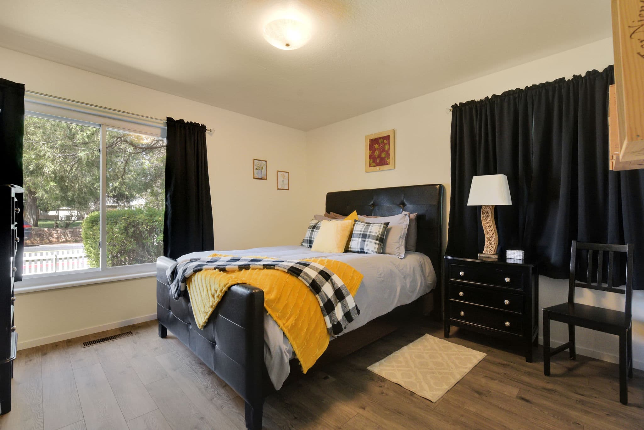 Cozy bedroom featuring a black bed, yellow and gray bedding, and a window with black curtains.