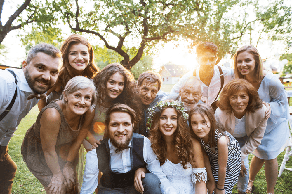 A joyful group of family and friends gathers outdoors, celebrating a wedding.