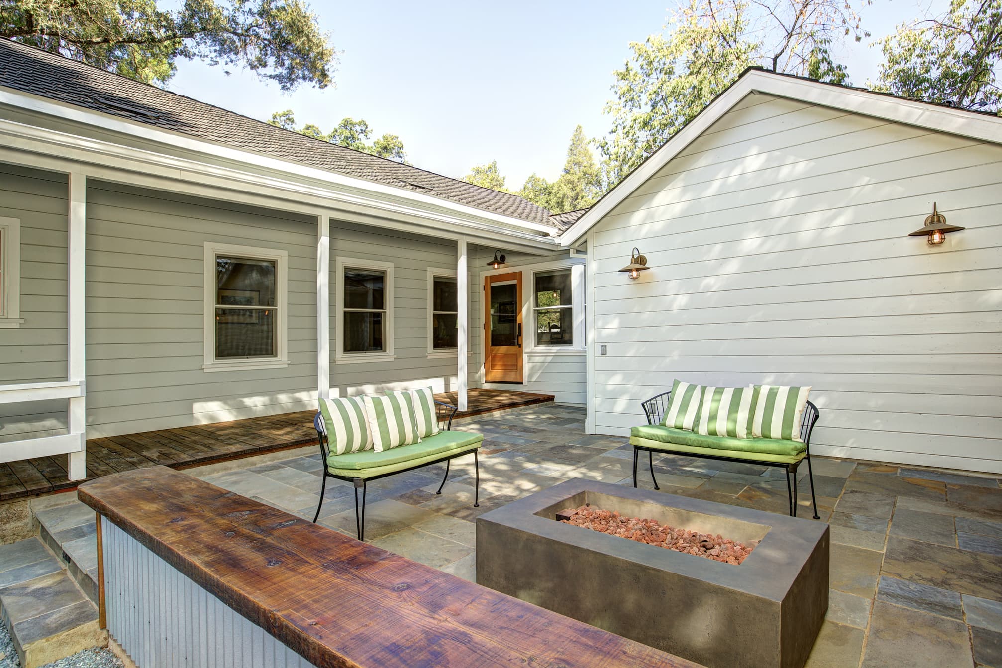 A cozy patio featuring two green-striped chairs, a fire pit, and a modern home exterior.