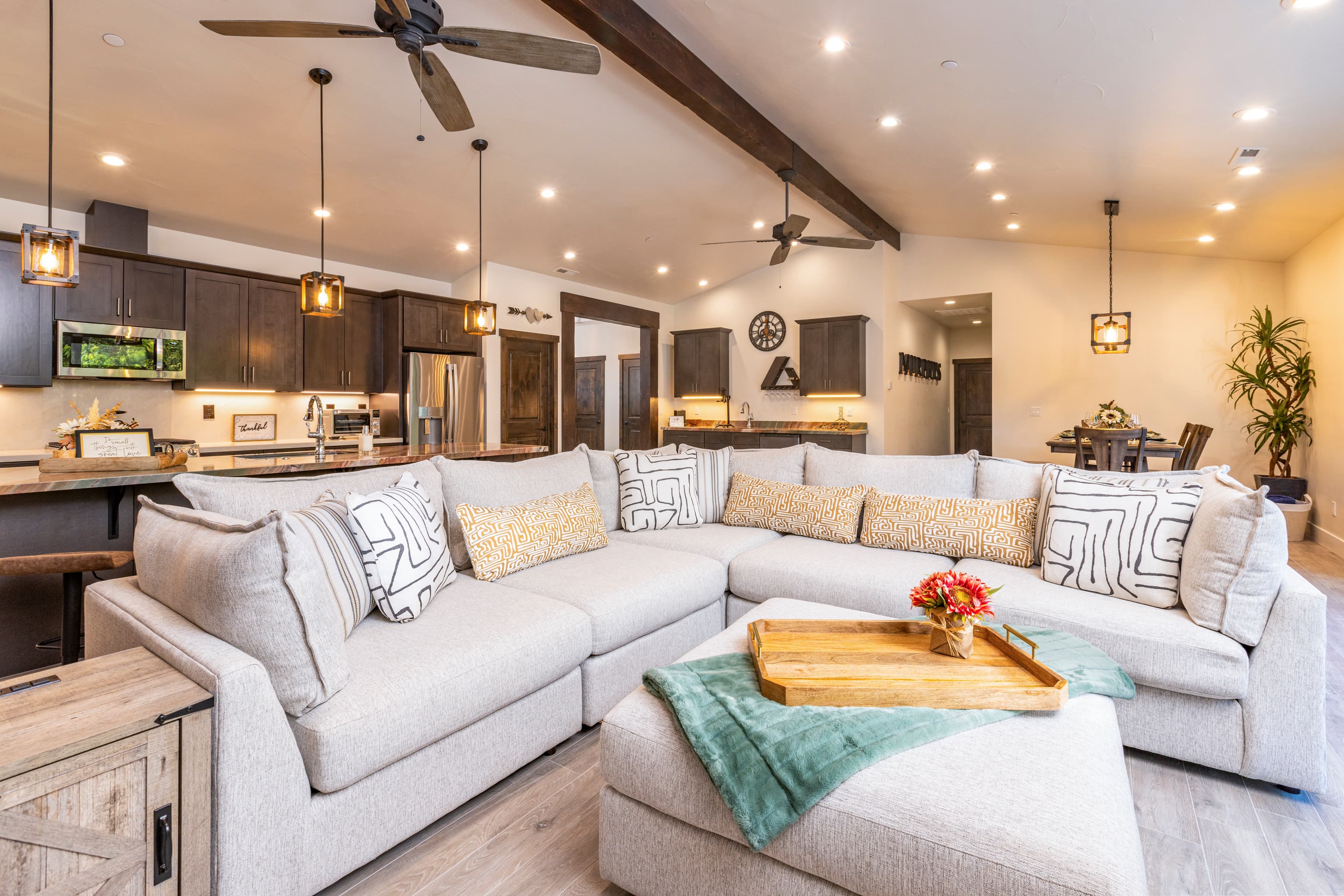 A modern living room features a spacious sectional sofa, a wooden coffee table, and an open kitchen in the background.