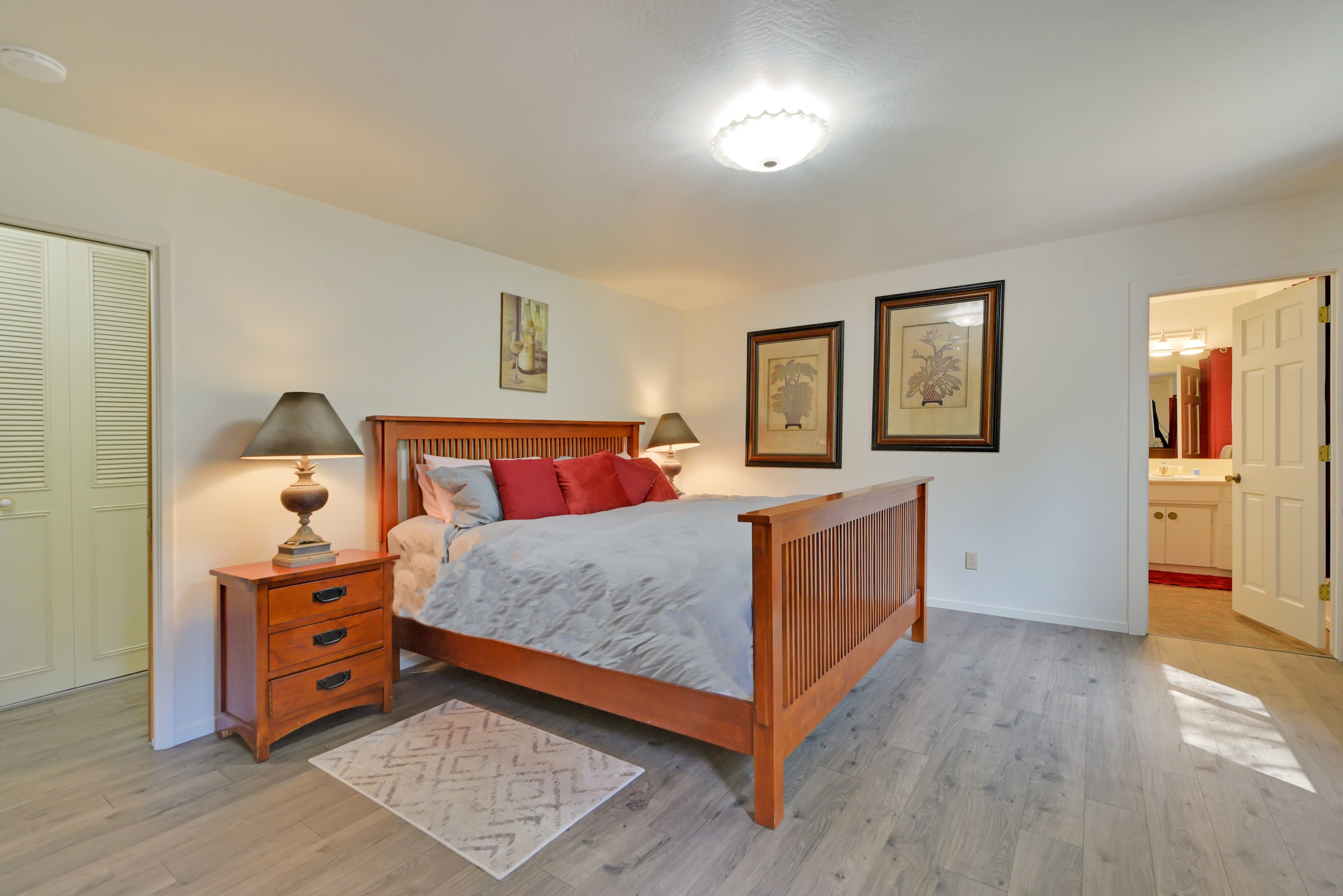 A cozy bedroom featuring a wooden bed, nightstand with a lamp, and framed artwork on the walls.
