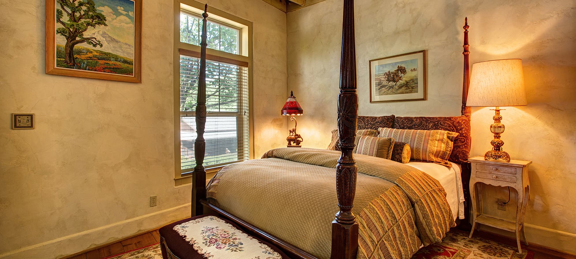 Cozy bedroom featuring a four-poster bed, warm lighting, and windows with a view.