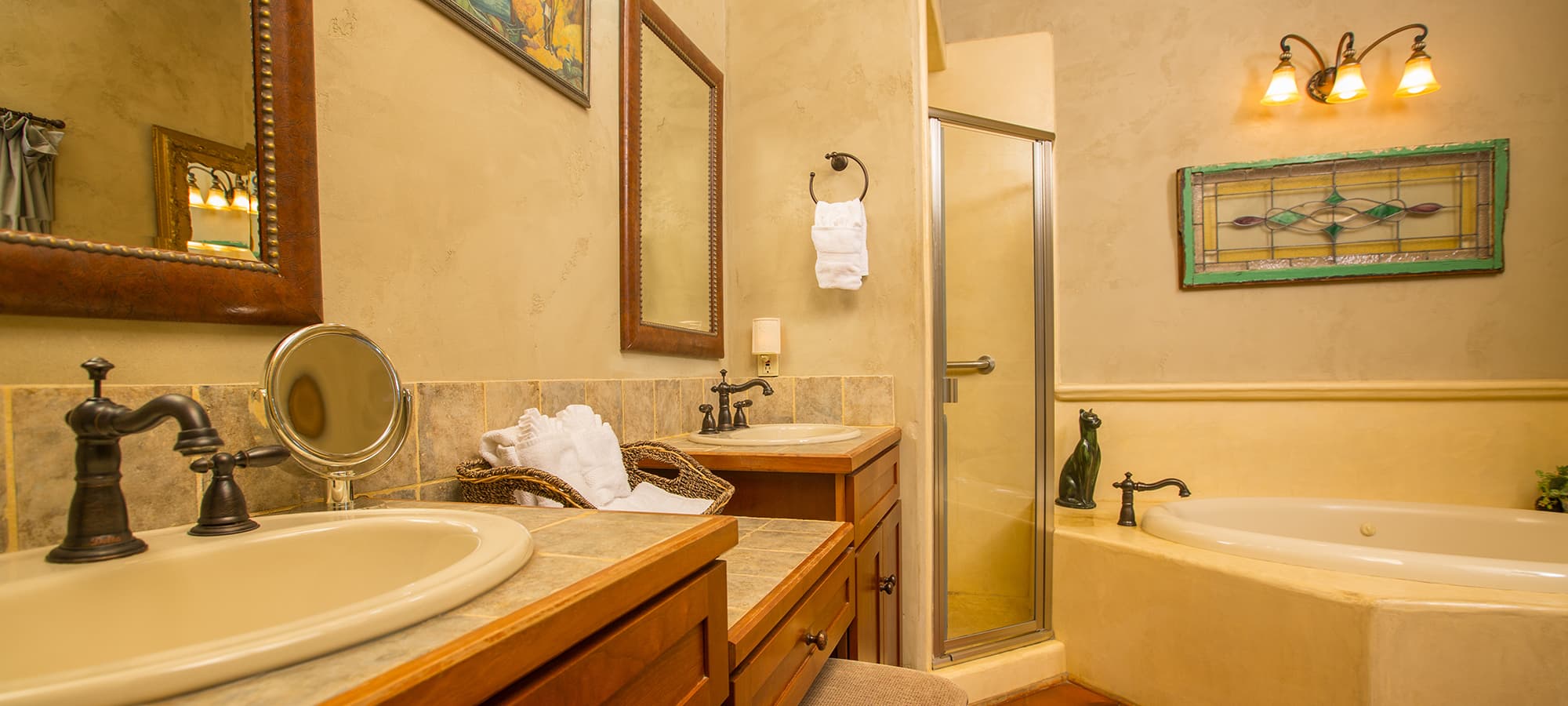 A well-lit bathroom featuring dual sinks, a shower, and a relaxing bathtub.