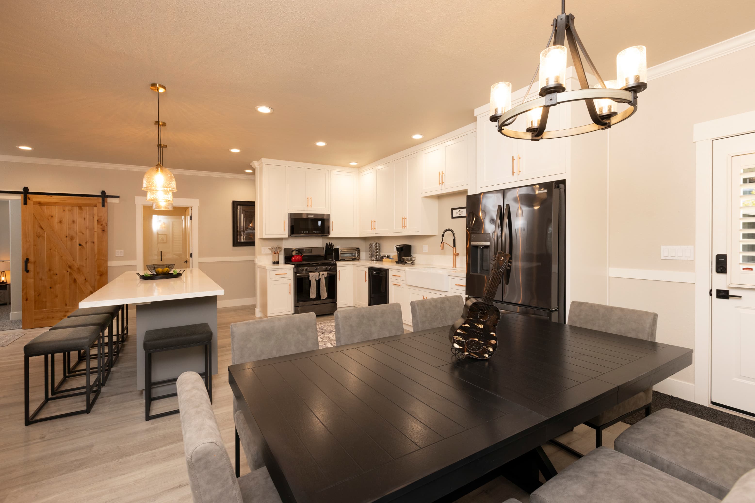 A modern kitchen and dining area featuring a large black table, gray chairs, and stainless steel appliances.
