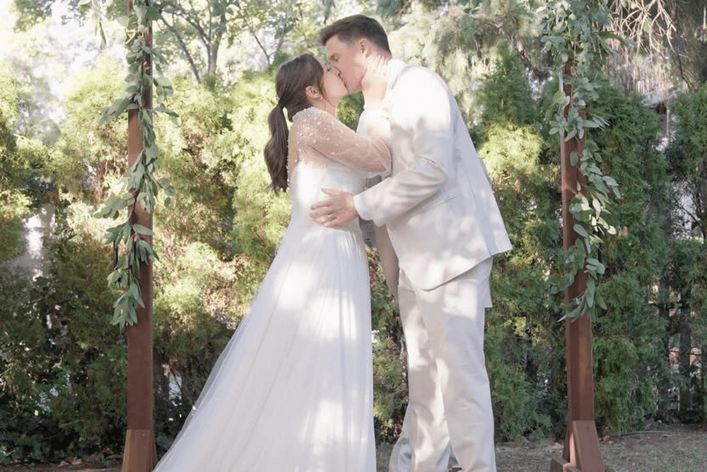 A bride and groom kiss under a floral arch during their wedding ceremony.
