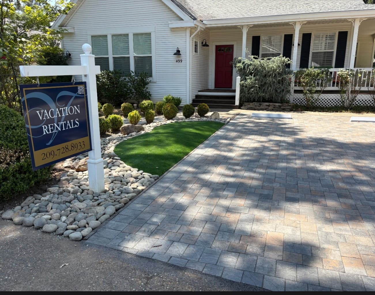 A welcoming vacation rental home with a sign, lush front yard, and paved driveway.