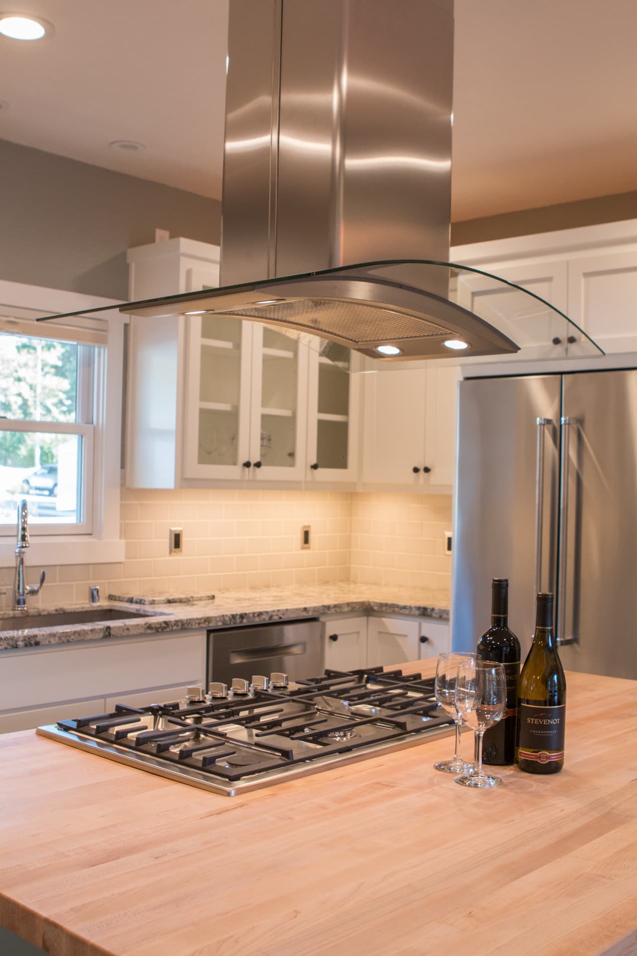 Modern kitchen with a gas stove, stainless steel hood, and bottles of wine on a wooden island.