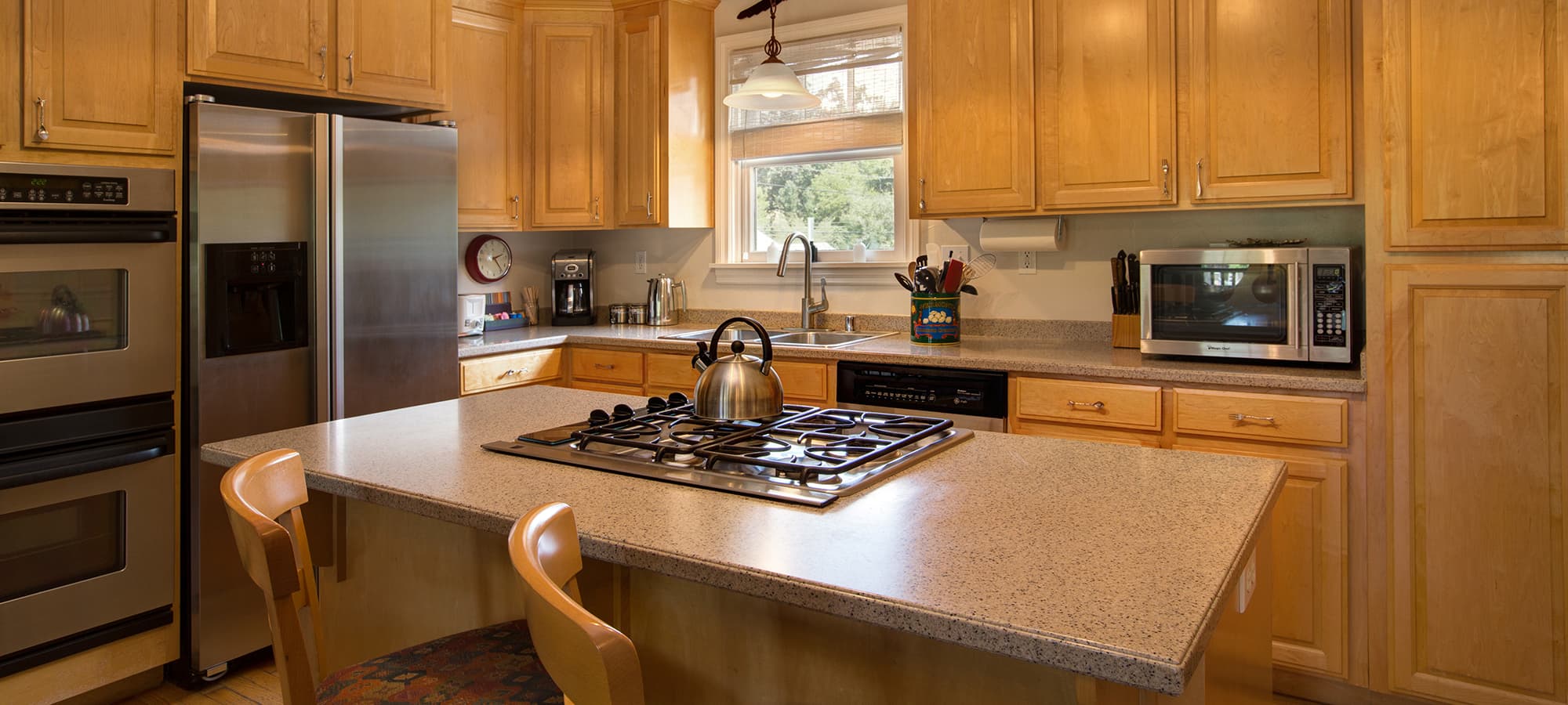 Modern kitchen featuring wooden cabinets, a central island with a stovetop, and stainless steel appliances.
