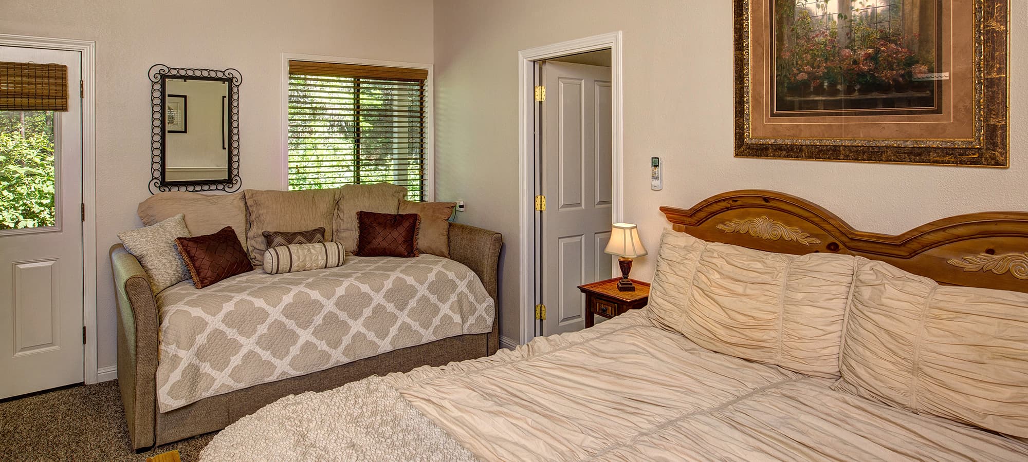 A cozy bedroom featuring a large bed, a twin daybed, and natural light from multiple windows.