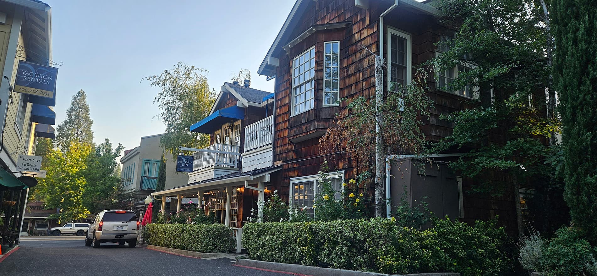 A charming wooden building with a blue awning, surrounded by greenery and parked cars.