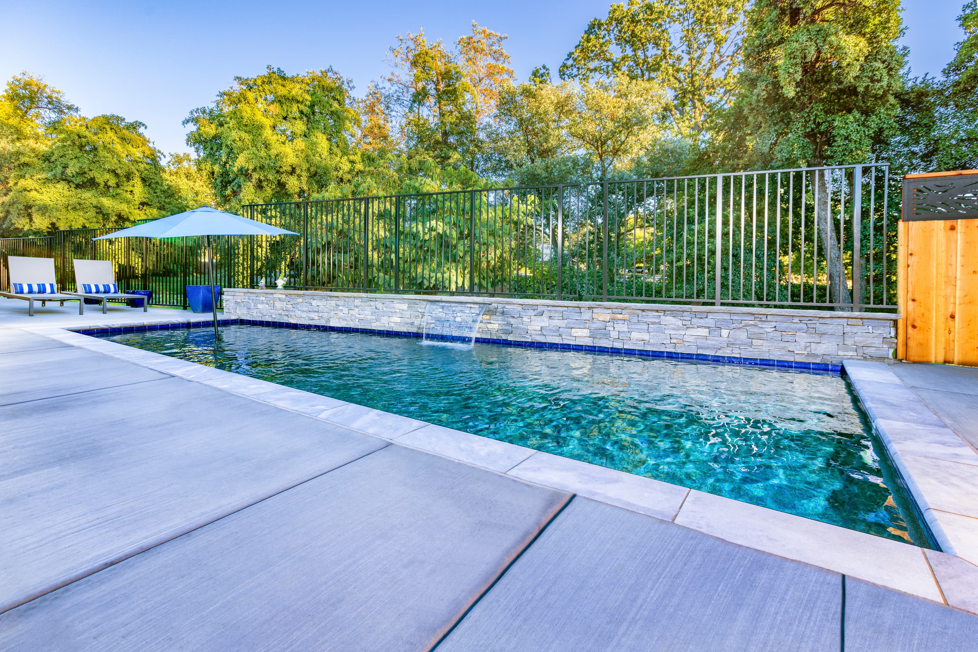 A tranquil swimming pool surrounded by lush greenery and a shaded area.