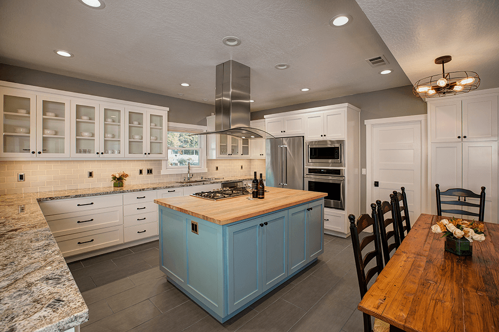 A modern kitchen featuring blue cabinetry, stainless steel appliances, and a wooden dining table.