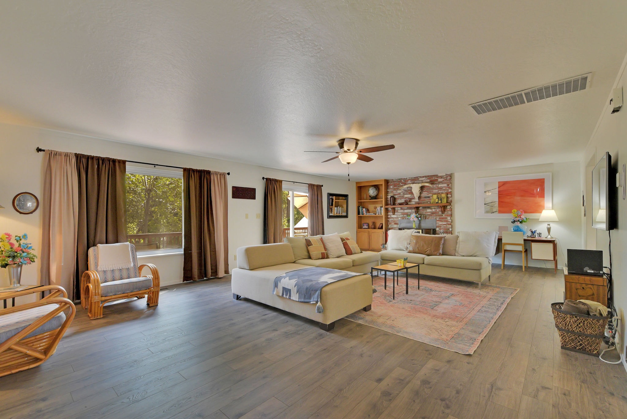 Spacious living room featuring a comfortable sectional sofa, light wood flooring, and large windows with curtains.