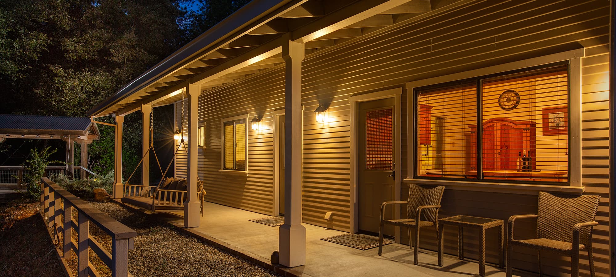 A well-lit porch of a house at night, featuring a swing and two chairs.