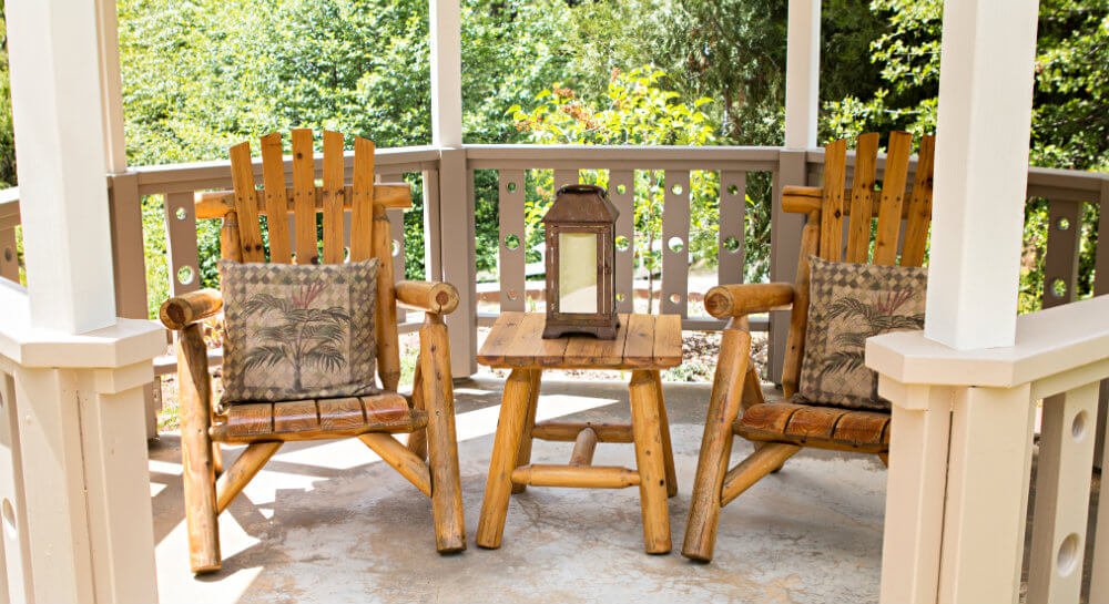 two wooden log chairs and small table with lantern in octagon gazebo with white fencing and posts