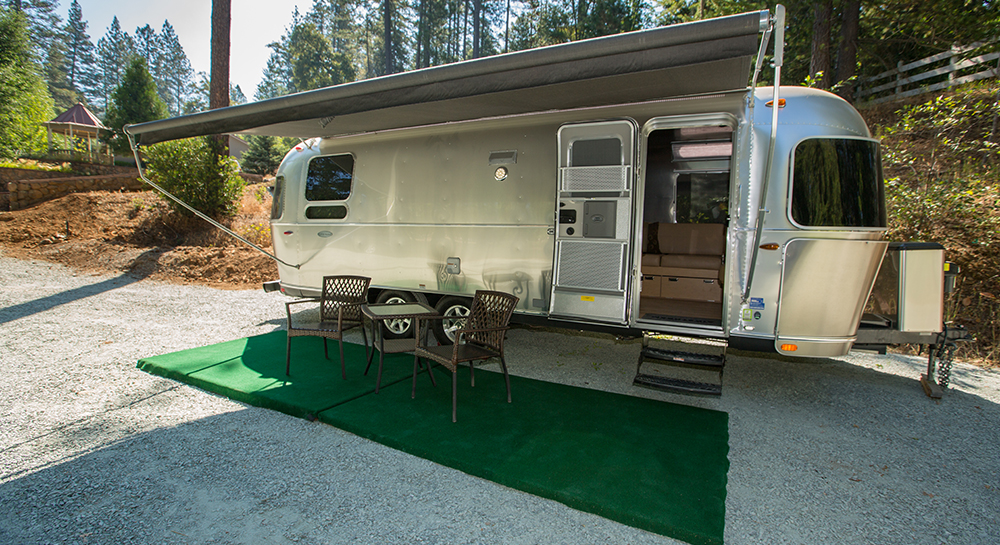 Exterior view of Windstream camper with canopy deployed over two paito chairs and table, with hill terrain in background accented by gazebo.