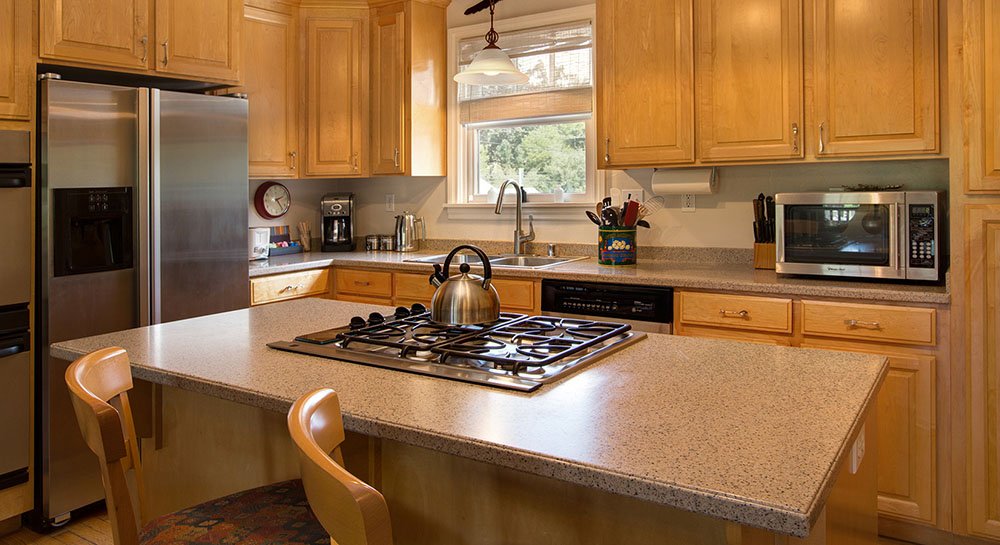 Kitchen with range on center island, and appliances on counter behind with open window above sink.