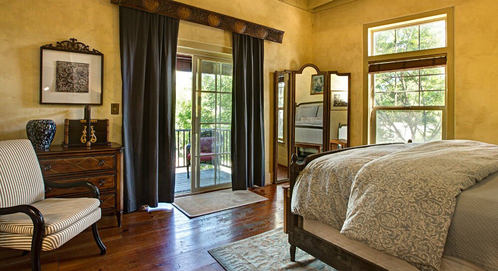 view toward sliding glass doors with blue curtains across foot of bed with grey cover, white and dark striped side chair