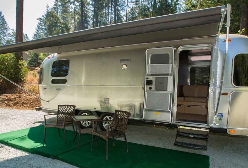 Exterior view of Windstream camper with canopy deployed over two paito chairs and table, with hill terrain in background accented by gazebo.