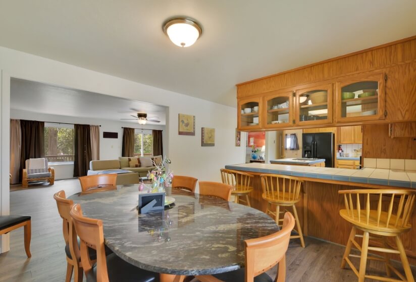 An open floor plan country kitchen and dining room with wood cupboards, tile countertops, and a granite tabletop with wood chairs.