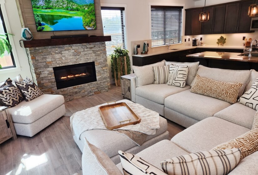 An open floor plan modern living room and kitchen with comfortable furnishings and a fireplace with a large flat screen tv above the mantle.